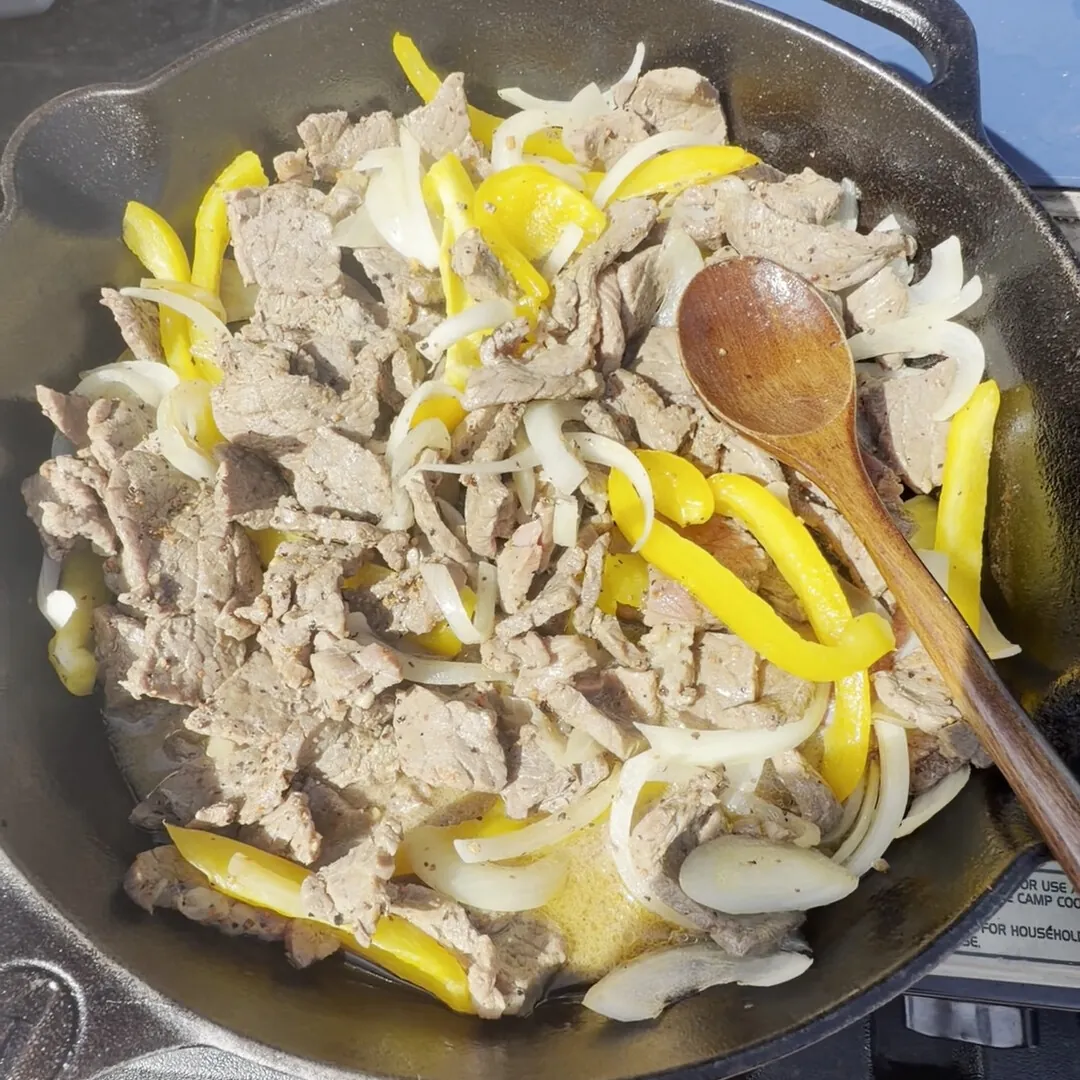 Steak, peppers and onions cooking in a cast iron pan