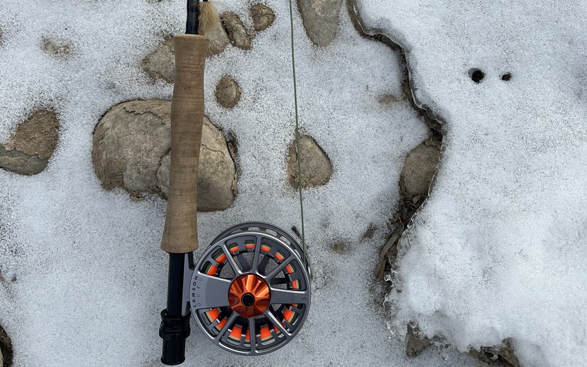 A fly rod and reel lying on snowy river rocks